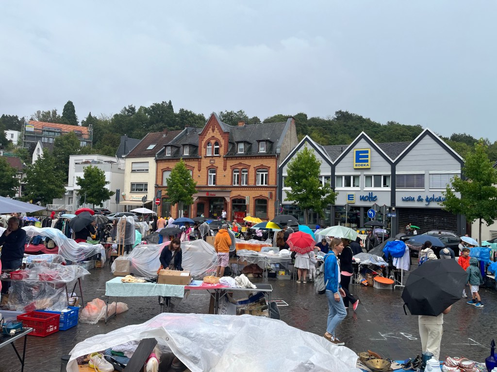 Menschen in Regenkleidung mit Regenschirmen beim
Flohmarkt auf dem Hofgartenplatz in Wiesbaden-Sonnenberg