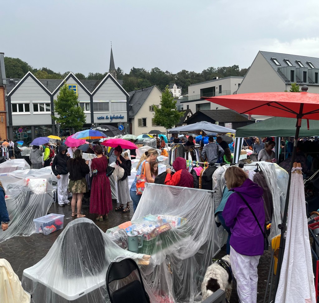 Menschen in Regenkleidung mit Regenschirmen beim
Flohmarkt auf dem Hofgartenplatz in Wiesbaden-Sonnenberg
